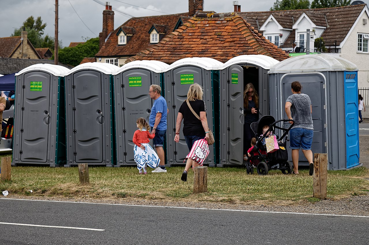 Een rij blauwe mobiele toiletcabines op een festivalweide