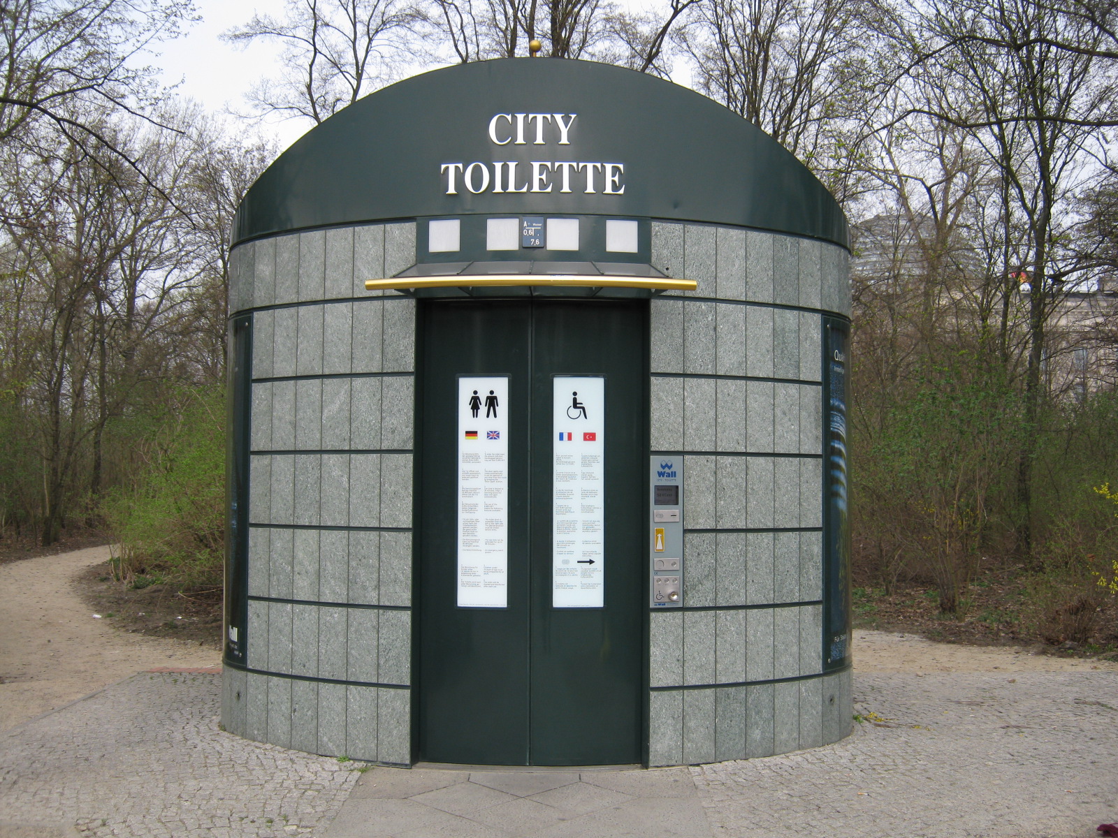 Een groene ronde straattoiletcabine met het opschrift City Toilette en een betaalzuil met muntgleuf naast de deur